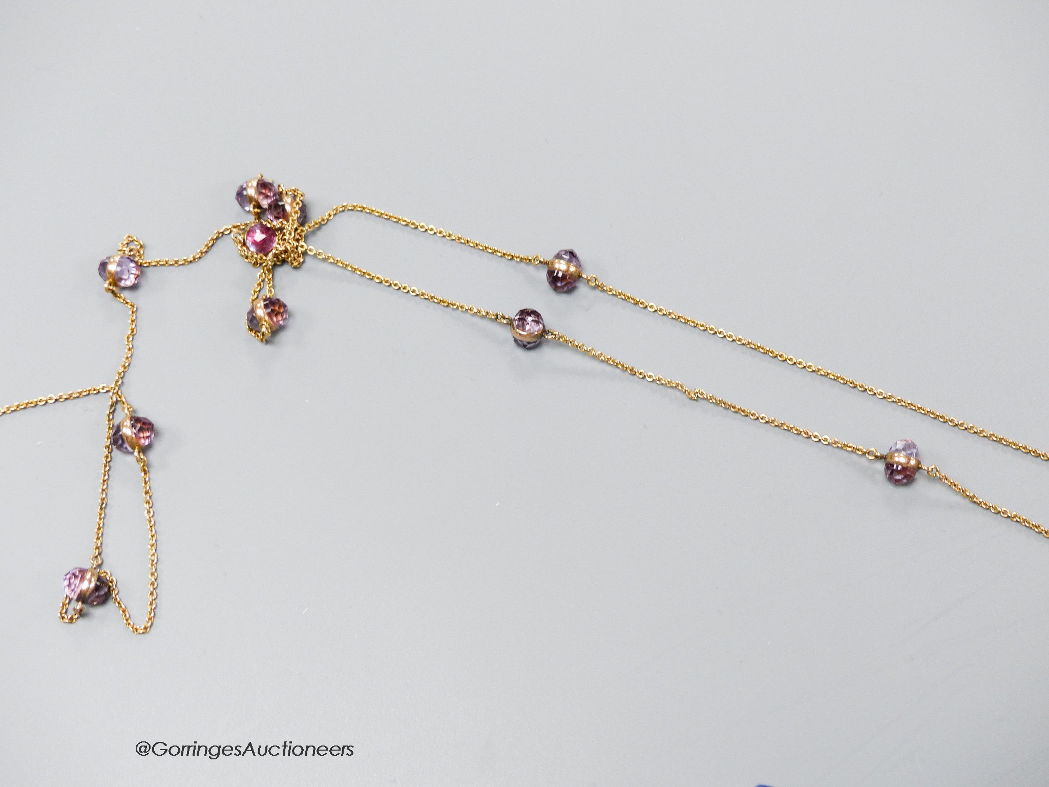 A yellow metal (stamped 14k) and facet cut purple stone set guard chain, 98cm, (link has become detached), gross weight 11.7 grams.